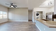 This single-floor unit offers a clean, contemporary design highlighted by light wood-look flooring and neutral warm-gray walls that flow consistently throughout the space. The open-concept living area is generously proportioned, featuring elevated ceilings, a sleek black ceiling fan, and large windows with a sliding glass door that invite abundant natural light and outdoor views. Vertical blinds provide privacy control at the patio access point.

The kitchen is well-appointed with white shaker-style cabinetry, light-toned countertops, a subtle gray tile backsplash, and a full suite of stainless steel appliances including a range, over-the-range microwave, and dishwasher. An extended kitchen peninsula with an undermount sink serves as a natural divider between the kitchen and living areas. A dedicated in-unit laundry nook accommodates a stacked washer and dryer.

The bedroom features its own ceiling fan and a window with natural light. The primary bathroom includes a white vanity with warm countertops, a framed mirror, and a tiled walk-in shower, with an adjacent walk-in closet featuring built-in shelving. A second bathroom mirrors the clean aesthetic with a white vanity and shower/tub combination.