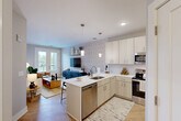 Located at 700 N Second St in Brighton, MI, this thoughtfully designed one-bedroom, one-bathroom residence offers a clean, modern aesthetic across a single floor. The open-concept kitchen and living area serves as the heart of the home, where a well-appointed kitchen features floor-to-ceiling white cabinetry, a herringbone tile backsplash, stainless steel appliances including a range, microwave, dishwasher, and refrigerator, and a peninsula with quartz countertops and bar seating. Pendant lighting and recessed fixtures provide both task and ambient illumination throughout. The living area flows naturally from the kitchen, accented by patterned wallpaper, light hardwood-style flooring, and French doors that open to a private balcony with outdoor views. The bedroom offers plush carpeting, neutral tones, and generous natural light through large windows, creating a calm retreat. A dedicated closet provides ample storage. The bathroom is finished with a quartz-topped vanity, light wood cabinetry, and a full soaking tub with shower. In-unit laundry adds everyday convenience. The overall ambiance is contemporary and cohesive, combining functional design with stylish finishes throughout.