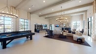 Located at 728 N Church St in Spartanburg, SC, this single-floor community clubhouse offers a sophisticated and welcoming atmosphere defined by soaring vaulted ceilings with exposed beams and large-format tile flooring throughout. The open-concept layout is anchored by a generous social lounge area furnished with plush sectional seating, accent chairs, and a central coffee table arranged around a dark fireplace — all illuminated by dramatic tiered ring chandeliers that serve as striking focal points overhead.

The game area features a full-size pool table and a shuffleboard table positioned near floor-to-ceiling windows dressed in elegant geometric-patterned drapery, flooding the space with natural light and offering views of the surrounding community. A built-in bar and lounge counter with bar seating and open shelving provides a dedicated space for casual gatherings and entertaining.

A dedicated business center offers a long wooden desk with desktop computers and a private bistro-style seating nook beside a tall window — ideal for residents working remotely. Throughout the space, neutral tones of cream, taupe, and charcoal are paired with warm wood accents, creating a refined yet comfortable ambiance. Direct exterior access connects the clubhouse seamlessly to the outdoor community grounds.