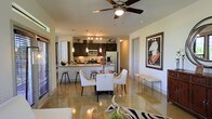 This single-floor residence offers a seamless open-concept layout that integrates the living, dining, and kitchen areas into one cohesive and inviting space. The polished concrete floors reflect light throughout, lending the interior a sleek, modern aesthetic that ties the entire floor plan together.

The kitchen is well-appointed with dark espresso cabinetry, stainless steel appliances including a French door refrigerator and range, a tile backsplash, and granite or stone countertops. A raised breakfast bar provides casual seating with bar stools, making it a practical and social hub of the home. Pendant lighting hangs above the kitchen area, adding warmth and a designer touch.

The dining area sits adjacent to the kitchen and features a round dining table surrounded by elegant white upholstered chairs, creating a refined yet comfortable setting for meals and entertaining. A ceiling fan with a light fixture is centrally positioned overhead, contributing both function and style to the space.

Wall art and carefully chosen accessories, including a zebra-print area rug in the living zone, add personality and visual interest. The layout allows for natural light to filter through, enhancing the bright and airy feel of the interior. Overall, the space presents a polished and cohesive living environment with contemporary design sensibilities throughout.