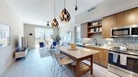 Located at 525 NE Seventh St in Fort Lauderdale, this contemporary 2-bedroom, 2-bathroom residence offers a thoughtfully designed open-concept floor plan with high-end finishes throughout. The combined living, dining, and kitchen area serves as the heart of the home, anchored by a striking kitchen featuring warm wood cabinetry, a mosaic tile backsplash, quartz countertops, stainless steel appliances, and a central island with bar seating illuminated by geometric pendant lighting. The living area flows seamlessly to a private balcony through floor-to-ceiling sliding glass doors, offering expansive views of the Fort Lauderdale skyline under abundant natural light. Light wood-style flooring runs throughout the main living spaces, complementing the neutral, contemporary palette. The spacious primary bedroom features city views through a large window, while both bedrooms are generously proportioned with ample closet space, including multiple walk-in closets with built-in shelving. The bathrooms are finished with large-format tile, including a glass-enclosed walk-in shower. An in-unit laundry room adds everyday convenience. The residence also benefits from a well-connected hallway layout that ensures privacy between the bedrooms and living spaces.