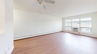 This 1-bedroom, 1-bathroom unit in Monona, Wisconsin offers a practical and comfortable layout across a single floor. The living room is bright and open, featuring warm hardwood-style flooring, a ceiling fan, baseboard heating, and a large window fitted with an in-unit AC unit that fills the space with natural light. The open layout connects seamlessly to the kitchen, which features warm wood-toned cabinetry, a white appliance suite, and a pass-through counter that enhances the sense of connectivity between rooms. The bedroom is a comfortable size, finished with plush neutral carpeting, a ceiling fan, and a row of horizontal windows that allow in soft, diffused light. A spacious sliding-door closet provides ample storage. The bathroom is a standout feature, showcasing classic retro character with sage green tile wainscoting, a mosaic tile floor, a white vanity with wood cabinet base, and a full bathtub with shower combination. Throughout the unit, crisp white walls and clean lines create a bright, neutral backdrop that is easy to personalize. Baseboard heating is present throughout, ensuring comfort during Wisconsin winters. The overall ambiance is clean, functional, and move-in ready.