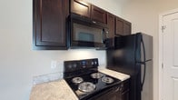 Located at 1655 Gilmore Park Ave in Columbus, Ohio, this single-floor residence offers a thoughtfully designed living space with a focus on functionality and modern aesthetics. The kitchen stands out as a highlight of the home, showcasing rich, dark espresso-toned cabinetry with raised-panel detailing that extends to the ceiling, maximizing storage capacity. The cabinetry is complemented by a suite of black Whirlpool appliances, including an electric range with coil burners, an over-the-range microwave with integrated ventilation, and a full-size refrigerator. The countertops feature a light marbled finish that provides a striking contrast against the dark cabinetry and appliances, creating a bold yet cohesive visual palette. The neutral-toned walls contribute to a clean, bright atmosphere throughout the kitchen. The overall design reflects a practical yet stylish approach, with durable finishes and a layout that supports everyday living with ease. The single-floor layout ensures convenient accessibility throughout the home, making it a comfortable and efficient space suited for a variety of lifestyles.