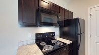 Located at 1655 Gilmore Park Ave in Columbus, Ohio, this single-floor residence offers a thoughtfully designed living space with a focus on functionality and modern aesthetics. The kitchen stands out as a highlight of the home, showcasing rich, dark espresso-toned cabinetry with raised-panel detailing that extends to the ceiling, maximizing storage capacity. The cabinetry is complemented by a suite of black Whirlpool appliances, including an electric range with coil burners, an over-the-range microwave with integrated ventilation, and a full-size refrigerator. The countertops feature a light marbled finish that provides a striking contrast against the dark cabinetry and appliances, creating a bold yet cohesive visual palette. The neutral-toned walls contribute to a clean, bright atmosphere throughout the kitchen. The overall design reflects a practical yet stylish approach, with durable finishes and a layout that supports everyday living with ease. The single-floor layout ensures convenient accessibility throughout the home, making it a comfortable and efficient space suited for a variety of lifestyles.
