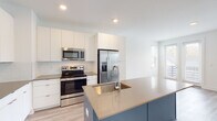 Located at 45 Boynton Ave SE in Atlanta, Georgia, this modern three-story home offers a well-designed layout with clean lines and contemporary finishes throughout. The ground level includes an attached garage with a sectional door, concrete flooring, and an electrical panel, providing secure and convenient parking or additional storage space.

The main living level showcases an open-concept kitchen and living area bathed in natural light from large windows. The kitchen is a standout feature, boasting sleek white flat-panel cabinetry extending to the ceiling, a subway tile backsplash, quartz countertops, and a striking blue center island with an undermount sink. Stainless steel appliances, including a French door refrigerator, range, and microwave, complete the modern aesthetic. Light wood-look flooring runs throughout this level, adding warmth to the space. A convenient half bathroom with a wood-toned vanity and white cabinetry is also found on this floor.

The upper floors feature carpeted bedrooms filled with natural light, including a room with an en-suite bathroom and a walk-in closet with built-in shelving. Carpeted staircases with white railings and a barn-style door accent connect all three levels, contributing to the home's modern yet approachable character. Recessed lighting throughout ensures a bright and inviting ambiance in every room.