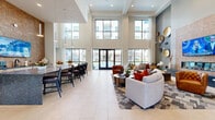 Located at 12631 Vance Jackson Rd in San Antonio, TX, this impressive amenity center spans a generously proportioned single floor, offering residents a comprehensive and upscale community experience. The entrance greets visitors with soaring double-height ceilings and dramatic floor-to-ceiling steel-framed glass doors that flood the space with natural light, setting an elegant and welcoming tone throughout.

The main lounge area features a striking accent wall clad in hexagonal mosaic tile, anchored by a sleek linear fireplace and a large mounted television — an ideal gathering space with refined furnishings and an airy ambiance. Adjacent seating nooks provide quieter retreats, adorned with vibrant artwork, large windows overlooking lush landscaping, and plush, contemporary furniture.

The fitness center is expansive and well-appointed, housing a full array of strength and cardio equipment, including treadmills, cycling bikes, stair climbers, and cable machines, all complemented by floor-to-ceiling mirrors and flat-screen televisions. Natural light pours in through wide windows framing views of the courtyard and palm trees.

Outdoors, a resort-style pool and spa serve as the centerpiece of the courtyard, surrounded by lounge chairs, umbrella-shaded seating, decorative fountains, and lush landscaping. The multi-story building architecture, featuring brick and stucco facades with private balconies, creates a vibrant and enclosed outdoor environment. A dedicated game room and utility room round out the functional offerings of this exceptional amenity space.