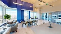 Located on an upper floor of a Calgary high-rise, this social room at 850 11 St SW offers a dynamic communal space designed for gathering and entertaining. The interior is immediately striking, defined by bold cobalt and violet accent walls adorned with geometric patterns that extend across the ceiling, creating an energetic and modern atmosphere.

Floor-to-ceiling windows wrap around the space, flooding the interior with abundant natural light and framing sweeping panoramic views of the Calgary cityscape and surrounding landscape. The large-format tile flooring provides a clean, polished base that complements the vivid color palette throughout.

The main gathering area accommodates multiple dining tables paired with industrial-style metal chairs, offering ample seating for groups of various sizes. A dedicated lounge corner features plush upholstered armchairs positioned to take full advantage of the expansive city views, making it an ideal spot for casual conversation or relaxation.

The full kitchen is thoughtfully appointed with wood-grain cabinetry, stainless steel appliances including a French door refrigerator and wall oven, a cooktop with a ventilation hood, and a striking quartz waterfall island with bar seating. Lush indoor plants are positioned throughout, adding a refreshing natural contrast to the urban, design-forward interior. Pendant and linear fixtures provide layered lighting across the entire space.