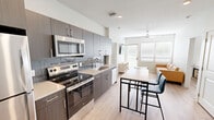 Located at 576 W Center St in Fayetteville, Arkansas, this single-floor residence offers a thoughtfully designed layout with 2 bedrooms and 2 bathrooms. The interior features light wood-tone flooring throughout, neutral walls, and ceiling fans in every room, creating a bright and cohesive aesthetic.

The kitchen is a standout feature, showcasing dark espresso cabinetry, a blue subway tile backsplash, light quartz countertops, and a full suite of stainless steel appliances including a refrigerator, range, microwave, and dishwasher. A bar-height dining table with seating sits adjacent to the kitchen, making the space functional and social.

The living room is filled with natural light from large windows fitted with horizontal blinds, and opens directly to a private balcony with outdoor views of surrounding greenery. Durable wood-look flooring and a ceiling fan add comfort and practicality.

Both bedrooms are well-proportioned, each with a window for natural light, ceiling fans, and ample floor space. The primary bedroom connects to a bathroom featuring a glass-enclosed shower, a dark-cabineted vanity, and light countertops. The second bathroom includes a tub-shower combination and a matching vanity. A hallway and closet round out the efficiently organized floor plan.