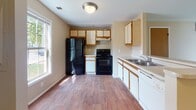 This two-floor residence offers a straightforward and functional layout designed to maximize comfort and usability. The main level features an open living area with neutral-toned carpet and warm beige walls, creating a bright and welcoming atmosphere. A staircase leads to the upper level, while a pass-through counter connects the living space to the kitchen, enhancing the sense of openness. Natural light enters through multiple windows, offering views of surrounding greenery.

The kitchen is equipped with white cabinetry accented by oak trim, light-toned countertops, a stainless steel sink, and black appliances including an electric range and refrigerator. Wood-style flooring runs throughout the kitchen, adding warmth and durability to the space.

Both bedrooms are located on the upper level, each featuring plush carpeting, neutral walls, and windows that bring in natural light. The shared full bathroom includes a combined tub and shower, a single-sink vanity with ample storage, a large mirror, and wood-style flooring that complements the overall aesthetic of the home. The layout is practical and well-suited for everyday living.