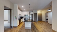 This well-appointed single-floor residence offers a thoughtfully designed layout with modern finishes throughout. The open-concept kitchen serves as the heart of the home, featuring white shaker cabinetry, a white subway tile backsplash, dark granite countertops, a center island with pendant lighting, and a full suite of stainless steel appliances including a French door refrigerator, electric range, built-in microwave, and dishwasher. Wood-look plank flooring flows seamlessly through the kitchen and living areas, creating a warm and cohesive aesthetic.

The bedrooms are carpeted for comfort, with one featuring a spacious walk-in closet equipped with built-in shelving and hanging rods, while another bedroom includes a standard closet. Large windows with horizontal blinds allow ample natural light into the sleeping areas, offering views of the surrounding exterior.

The primary bathroom provides a generous vanity with dark granite countertops, white cabinetry, and a large mirror, directly accessible from the bedroom. A secondary full bathroom features a similar white-cabinet vanity with dark countertops and a tiled shower-tub combination. A dedicated in-unit laundry room houses a full-size front-loading washer and dryer with overhead shelving for added storage convenience.