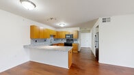 This single-floor residence offers a thoughtfully designed layout that balances functionality and comfort throughout its key living areas. The kitchen serves as a central highlight, showcasing warm honey-toned wood cabinetry, granite countertops, and a matching granite-topped peninsula ideal for casual dining or additional prep space. A speckled tile backsplash ties the design together, while black appliances—including a range, microwave, dishwasher, and refrigerator—provide a sleek contrast. Rich hardwood flooring extends through the kitchen, entryway, and living areas, lending warmth and visual continuity. The living room is bright and open, featuring a sliding glass door framed by vertical blinds that invite natural light and provide direct access to an outdoor green space. The entryway is clean and minimalist, with white walls and hardwood floors that set a welcoming tone upon arrival. The bedroom offers plush carpeting, a full-length bi-fold closet, and a neutral palette that creates a calm retreat. A second carpeted room provides additional flexible space. The bathroom is designed with accessibility in mind, equipped with grab bars, a wall-mounted sink, and a tub-shower combination with a handheld showerhead, all finished with neutral stone-look tile flooring. This residence presents a practical and comfortable living environment with consistent, quality finishes throughout.