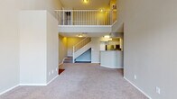 Located in Saint Petersburg, Florida, this two-story residence offers a well-designed layout that balances open communal spaces with private upper-level accommodations. The living area immediately impresses with soaring double-height ceilings and a carpeted floor, creating an expansive, airy atmosphere. Large French doors flood the space with natural light and provide outdoor access, while a white-railed staircase and upper-level balcony add architectural interest and visual depth to the interior.

The kitchen is efficiently laid out in a galley style, featuring stainless steel appliances including a full-sized refrigerator and range, white cabinetry, a light tile backsplash, and rich hardwood-style flooring. A breakfast bar peninsula connects the kitchen to the living area, making it ideal for casual dining or entertaining. Hardwood-style flooring continues throughout the kitchen and bathrooms, providing a warm contrast to the plush carpeting found in the living and bedroom areas.

The bathrooms are finished with white vanity cabinetry, clean countertops, large mirrors, and tiled shower-tub combinations. Bedrooms are generously proportioned, carpeted, and well-lit by natural light through blinded windows. The primary bedroom features a connected en-suite bathroom, adding a layer of privacy and convenience. Overall, the home presents a clean, neutral palette throughout.