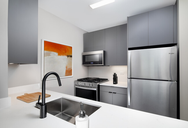 Renovated Package II kitchen with white quartz countertop and backsplash, upgraded stainless steel appliances, upgraded black hardware, and upgraded lighting - Avalon Midtown West