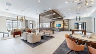Located at 10141 E Williams Field Rd in Mesa, AZ, this thoughtfully designed amenity lounge spans a generously proportioned single floor, offering a sophisticated and multifunctional community gathering space. The open-concept layout is anchored by large-format stone-look tile flooring that flows seamlessly throughout, unifying each distinct zone within the space.

The main lounge area features multiple curated seating arrangements, including plush neutral sofas and accent chairs, illuminated by striking gold pendant light fixtures and recessed lighting. A wood-slatted architectural partition serves as a design centerpiece, visually defining zones while maintaining an airy, connected feel. Adjacent to the lounge sits a stylish wet bar with counter seating, backlit shelving, and wall-mounted displays.

A dedicated games area houses a solid wood billiards table set beneath dramatic pendant lighting, complemented by built-in shelving with warm accent lighting. Nearby, a lounge nook features a linear fireplace, a wall-mounted TV, and bold terra-cotta accent chairs, creating an intimate retreat within the larger space.

The dining area offers round and rectangular tables beneath oversized pendant lights, positioned near floor-to-ceiling windows that invite natural light. A co-working room with glass partition doors, a round conference table, and exterior views rounds out this well-appointed, design-forward community space.