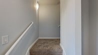 This multi-level residence is thoughtfully distributed across four floors, offering a well-organized layout that separates living and sleeping spaces. The entry level provides a compact but functional introduction to the home, leading upward via carpeted staircases accented with white railings and wall-mounted lighting.

The main living floor encompasses an open-plan kitchen and living area. The kitchen is a standout feature, equipped with warm maple cabinetry, dark granite countertops, a tile backsplash, stainless steel appliances including a range, microwave, and French door refrigerator, and a central island with an undermount sink. Pendant and track lighting illuminate the space, complemented by natural light from a nearby window. The adjacent living area features rich hardwood flooring and dual windows with views of surrounding greenery.

The upper level hosts both bedrooms, each carpeted and fitted with ceiling fans. The spacious primary bedroom benefits from multiple windows that frame outdoor views. The second bedroom offers a similarly comfortable feel. Three closets throughout the home, including a well-lit walk-in, provide generous storage. Both bathrooms feature tile flooring and tub-shower combinations with tiled surrounds, maintaining a clean, neutral aesthetic throughout.