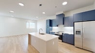 Located at 501 Orleans St in Richmond, VA, this contemporary two-bedroom, two-bathroom residence offers a thoughtfully designed single-floor layout with modern finishes throughout. The open-concept kitchen and living area serves as the heart of the home, showcasing bold navy-blue cabinetry, a large white quartz waterfall island with an undermount sink, stainless steel appliances, and sleek pendant lighting — all set against warm light wood-style flooring that extends through the main living areas. The bright, airy atmosphere is enhanced by recessed lighting and clean white walls. The primary bedroom is generously sized, featuring plush carpet, a ceiling fan, and expansive windows that frame outdoor views and fill the room with natural light, with direct access to a private balcony. The second bedroom also enjoys natural light through a large window and continues the light hardwood flooring. Both bathrooms are finished with navy vanities, white quartz countertops, brushed nickel fixtures, and large-format tile flooring; one includes a tub-shower combination. Additional highlights include two closets, a dedicated in-unit laundry area, and a private balcony, making this a well-appointed and functional modern residence.