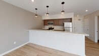 This single-floor unit at 242–244 Alexander St in Rochester's vibrant East End district offers a thoughtfully designed, modern interior with a clean, neutral aesthetic throughout. Light hardwood flooring extends across the main living areas, complementing the crisp white walls and creating a bright, cohesive atmosphere.

The open-concept living area is anchored by large windows and glass French doors that frame views of the surrounding cityscape, flooding the space with abundant natural light. The kitchen features a peninsula with pendant lighting overhead, rich dark wood cabinetry, light stone-toned countertops, and stainless steel appliances including a range, microwave, dishwasher, and refrigerator. A galley-style layout provides generous counter space and storage.

The bedrooms maintain the same light hardwood flooring and neutral palette, with windows that invite additional natural light and urban views. The bathroom is designed with accessibility in mind, incorporating a walk-in roll-in shower with grab bars, a handheld showerhead, light tile flooring, a vanity with a framed mirror, and recessed lighting. The overall ambiance is modern, clean, and well-lit, well-suited for comfortable urban living.