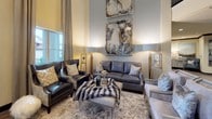This single-story commercial space presents a thoughtfully designed lobby and reception area that exudes sophistication. The entrance is immediately distinguished by dramatically soaring ceilings, accentuated by floor-to-ceiling drapery panels framing tall windows that invite generous natural light. The lounge area features rich charcoal leather seating, a plush fur-draped ottoman, and an ornate area rug, all anchored beneath a striking pair of abstract marble-toned art panels mounted high on the wall.

The reception area is anchored by a curved granite countertop in soft grey and white tones, paired with decorative wall paneling finished in a fluid, marble-inspired pattern. Recessed lighting and an arched ceiling detail lend the workspace an architectural elegance. The overall color palette throughout is warm and neutral, combining cream walls, dark wood trim, and wood-look flooring.

Accessibility is addressed with a conveniently located elevator and an ADA-compliant entry door situated along a well-appointed corridor with dark crown molding details. Together, these elements create a cohesive, upscale environment that balances professional functionality with refined, welcoming design.