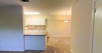 Located at 3500 Creighton Rd in Pensacola, Florida, this single-floor space offers a functional and comfortable layout designed for everyday living. The kitchen is a standout feature, equipped with white cabinetry, a stone tile backsplash, and light countertops that create a clean, bright aesthetic. A built-in sink and dishwasher add convenience, while a dark-topped breakfast bar or kitchen island provides additional prep and dining space. An elegant pendant light hangs above, adding a touch of style to the open layout. The kitchen flows seamlessly into the adjacent living area, which features warm, neutral carpet and soft, cream-toned walls that lend a cozy and inviting ambiance throughout. Recessed ventilation and ceiling-mounted lighting ensure the space is well-lit and comfortable. The open-concept design between the kitchen and living area promotes a sense of spaciousness, making the layout feel connected and easy to navigate. The overall aesthetic is clean and neutral, offering a versatile canvas well-suited for a variety of interior styles. This Pensacola residence combines practical features with a welcoming atmosphere in a convenient single-level layout.