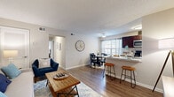 Located at 6139 Edward St in Norfolk, Virginia, this 2-bedroom, 2-bathroom single-floor residence offers a well-designed layout that maximizes comfort and functionality. The open-concept living and dining area serves as the heart of the home, featuring warm hardwood-style flooring, neutral walls, and a textured ceiling. The living room provides a welcoming atmosphere with ample space for seating and everyday living, while the adjacent dining area benefits from a large window that invites natural light and outdoor views.

The kitchen is equipped with rich dark cabinetry, light stone-finish countertops, stainless steel appliances including a refrigerator, range, and microwave, and a peninsula with bar seating that seamlessly connects to the main living space. A galley-style layout ensures efficient use of the kitchen's footprint.

The spacious primary bedroom features plush carpeting, a window with draping curtains, and a calm, neutral palette that promotes rest. The second bedroom mirrors this comfortable aesthetic, also with carpeted flooring and natural light. Both bedrooms offer generous space for furnishings. Two full bathrooms and a hallway with closet storage round out this thoughtfully arranged residence, providing practical convenience throughout.