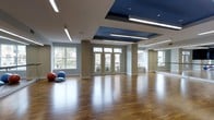 The Movement Studio at 100 Danforth Avenue in Dobbs Ferry, New York, is a thoughtfully designed fitness and wellness space that blends functionality with modern aesthetics. The studio occupies a single, open floor plan that provides ample room for a wide range of movement-based activities, from dance and yoga to group fitness classes.

The main studio floor is finished with rich, warm hardwood that extends throughout the space, offering both visual warmth and a performance-ready surface ideal for physical activity. The ceiling is a standout architectural feature, incorporating a bold navy blue recessed panel accented by sleek linear lighting fixtures that cast an even, inviting glow across the room. Recessed lighting further enhances the bright, energetic atmosphere.

Large windows along multiple walls flood the interior with abundant natural light while offering views of the surrounding outdoor environment, creating an airy, open feel. A full-length mirrored wall on one side of the studio supports movement practice and amplifies the sense of space. A ballet barre runs along the mirrored wall, making the studio well-suited for dance and barre-based workouts.

The neutral wall tones complement the vivid ceiling detail, resulting in a balanced and professional environment. Overall, the Movement Studio presents a polished, welcoming setting designed to inspire and support an active lifestyle.