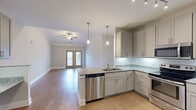 Located at 4531 Langdon Dr in Durham, NC, this well-appointed two-bedroom, two-bathroom residence offers a thoughtfully designed single-floor layout. The open-concept living area seamlessly combines the kitchen, dining, and living spaces, creating a bright and airy atmosphere. The kitchen is outfitted with granite countertops, gray shaker-style cabinetry, stainless steel appliances including a dishwasher and range, and pendant lighting over the peninsula. Light wood-look flooring flows throughout the main living areas. The living room features crown molding, a ceiling fan, and French doors that open onto a private balcony, allowing for excellent natural light. Both bedrooms are carpeted and include ceiling fans and windows with outdoor views. The primary bedroom offers a generous walk-in closet with wire shelving. The primary bathroom features a dual-sink vanity with granite countertops and gold-toned fixtures, while the second bathroom includes a tub-shower combination and a granite-topped vanity. Additional highlights include a pantry with built-in shelving, a dedicated laundry area, a utility room, and four closets providing exceptional storage. Crown molding and neutral tones throughout lend the space a clean, modern aesthetic.