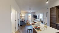 This single-floor residence showcases a thoughtfully designed open-concept layout with modern finishes throughout. The kitchen is a functional centerpiece, featuring wood-toned cabinetry extending to the ceiling, stainless steel appliances including a side-by-side refrigerator, electric range, and built-in microwave, complemented by white quartz countertops and a peninsula with bar seating. Track lighting illuminates the space, while wood-look plank flooring flows seamlessly throughout the unit.

The living area is generously proportioned, anchored by a ceiling fan and large sliding glass doors that open to a private balcony, filling the room with natural light and outdoor views. The open sightlines between the kitchen, dining, and living spaces enhance the overall sense of openness.

The primary bedroom features a ceiling fan, large windows with exterior views, and warm wood-look flooring. A second bedroom also benefits from natural light through a well-sized window. The bathroom offers a clean, contemporary aesthetic with wood-grain vanity cabinetry, a white quartz countertop, large-format tile flooring, and a full soaking tub with tiled surround. A closet with louvered doors provides additional storage near the entryway.