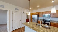 This single-floor residence offers a thoughtfully designed layout that balances functional living spaces with comfortable finishes throughout. The kitchen serves as the centerpiece of the home, showcasing a large island topped with speckled granite countertops and an undermount double sink. Warm-toned wood cabinetry lines the walls, complemented by a full suite of stainless steel appliances including a French door refrigerator with ice maker, an electric range, and an over-the-range microwave. Pendant lighting above the island adds a refined touch, while recessed lighting brightens the workspace. Durable wood-look flooring runs throughout the kitchen and connects seamlessly to the adjacent living areas. The living and bedroom spaces feature plush neutral carpeting, ceiling fans for year-round comfort, and windows fitted with blinds that allow natural light to filter in. A chandelier in one room adds an elegant accent. The full bathroom is generously proportioned, featuring a long vanity with wood cabinetry, a wide mirror, a toilet, and a combined tub and shower. Wood-look flooring continues here, tying the space together. The overall ambiance is clean, neutral, and move-in ready.