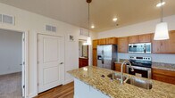 This single-floor residence offers a thoughtfully designed layout that balances functional living spaces with comfortable finishes throughout. The kitchen serves as the centerpiece of the home, showcasing a large island topped with speckled granite countertops and an undermount double sink. Warm-toned wood cabinetry lines the walls, complemented by a full suite of stainless steel appliances including a French door refrigerator with ice maker, an electric range, and an over-the-range microwave. Pendant lighting above the island adds a refined touch, while recessed lighting brightens the workspace. Durable wood-look flooring runs throughout the kitchen and connects seamlessly to the adjacent living areas. The living and bedroom spaces feature plush neutral carpeting, ceiling fans for year-round comfort, and windows fitted with blinds that allow natural light to filter in. A chandelier in one room adds an elegant accent. The full bathroom is generously proportioned, featuring a long vanity with wood cabinetry, a wide mirror, a toilet, and a combined tub and shower. Wood-look flooring continues here, tying the space together. The overall ambiance is clean, neutral, and move-in ready.