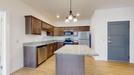 This single-floor residence offers a thoughtfully designed layout with a blend of functional and modern finishes throughout. The kitchen serves as a central highlight, showcasing rich dark-toned cabinetry with ample storage, granite-style countertops, and a full suite of stainless steel appliances including a refrigerator, electric range, built-in microwave, and dishwasher. A generously sized center island with a matching countertop provides additional workspace and casual dining potential. A pendant chandelier above the island adds a decorative touch, while recessed lighting ensures the space remains well-lit. Light hardwood-style flooring extends through the kitchen and entry areas, complementing the warm cabinetry tones. The living area features plush carpeting, a ceiling fan, and sliding glass doors that open to a private balcony with exterior views. A carpeted bedroom offers natural light through a window with neighborhood views. The bathroom includes a gray vanity, white countertop, framed mirror, and light hardwood-style flooring. Additional conveniences include a dedicated in-unit laundry room with a full-size washer and dryer, and a spacious walk-in closet with wire shelving.