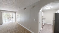 This single-floor residence offers a clean, functional layout designed for comfortable everyday living. The spacious living area is a standout feature, highlighted by plush carpet flooring, a ceiling fan, a textured ceiling, and a corner fireplace that serves as a natural focal point. Large sliding glass doors flood the space with natural light and provide access to an outdoor area, enhancing the open feel of the room. A graceful arched opening connects the living area to the kitchen, creating a cohesive flow between the two spaces. The kitchen is well-appointed with white shaker-style cabinetry, wood-toned laminate countertops, a stainless steel sink, and hardwood-style flooring, offering a bright and practical workspace. The bedroom is a comfortable retreat, featuring soft carpet, a window dressed with blinds that brings in natural light, and a ceiling fan for added comfort. The bathroom is neatly finished with a white vessel sink, wood-toned vanity, a full tub and shower combination with clean white tile surround, and a large mirror. Throughout the space, neutral tones and consistent finishes contribute to a cohesive and inviting ambiance.