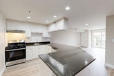 Located at 21 Kenmar Dr in Billerica, MA, this 2-bedroom residence offers a thoughtfully designed single-floor layout that maximizes functionality and comfort. The open-concept kitchen and living area serves as the heart of the home, showcasing a striking peninsula with dark granite countertops that contrast elegantly against crisp white cabinetry with decorative raised-panel detailing. Stainless steel appliances, a subway tile backsplash, and recessed lighting complete the kitchen's polished look. Light hardwood-style flooring runs seamlessly throughout the entire unit, creating a cohesive and airy feel. The living area benefits from a sliding glass door that opens to an outdoor view, allowing generous natural light to fill the space. Both bedrooms feature neutral warm-toned walls, recessed lighting, and built-in closets with bi-fold doors, offering practical storage solutions. One bedroom includes a window with outdoor views, enhancing its bright and welcoming atmosphere. A stacked washer and dryer unit is conveniently integrated within the residence. The overall design emphasizes clean lines, neutral tones, and modern finishes, creating a move-in-ready living environment.