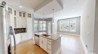 This well-appointed 2-bedroom, 3-bathroom residence in Durham, NC offers a functional and attractive single-floor layout. The open-concept kitchen is a standout, featuring white shaker cabinetry with glass-front upper panels, dark granite countertops, a decorative tile backsplash, stainless steel appliances, and a central island with a sink and built-in dishwasher — all illuminated by pendant lighting. Hardwood flooring flows throughout the main living areas, connecting the kitchen to a bright, airy living room lined with large bay windows that flood the space with natural light. Both bedrooms are carpeted and generously sized, with the primary bedroom offering access to a private en-suite bathroom complete with a tiled walk-in shower featuring a built-in bench and mosaic tile accent border. Each bedroom is served by well-organized closets with wire shelving systems. A dedicated laundry area houses a full-size top-loading washer. The private balcony provides serene views of a lush, wooded landscape with tall pines and open green space below. Neutral gray walls and clean white trim throughout create a cohesive, modern aesthetic suited for comfortable everyday living.