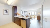 Located at 360 State St in the heart of New Haven, CT, this one-bedroom, one-bathroom residence offers a well-designed layout with modern finishes throughout. The open-concept kitchen and living area serves as the centerpiece of the space, featuring a peninsula island with a white quartz countertop, rich dark-wood cabinetry, stainless steel appliances including a refrigerator, microwave, and electric range, and white upper cabinets that brighten the space. The kitchen flows seamlessly into the living area, where light wood-tone flooring, crisp white walls, and large windows frame sweeping views of the New Haven skyline, filling the space with natural light. The generously sized bedroom continues the light and airy aesthetic, offering its own large window with city views, a walk-in closet, and light wood flooring. The bathroom is clean and functional, featuring tile flooring, a wood-toned vanity with a white sink, a mirrored medicine cabinet, and a shower-tub combination. Throughout the residence, the design balances contemporary style with practical functionality, creating a comfortable and visually cohesive living environment in one of New Haven's most prominent addresses.