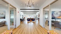 Located at 7430 N Silverbell Rd in Marana, Arizona, this thoughtfully designed single-floor community space offers an open-concept layout that seamlessly connects a living room, dining area, and kitchen. The interior is defined by soaring ceilings accented with striking dark wood beam details, crisp white walls, and warm light wood flooring throughout, creating a bright and welcoming atmosphere.

The living area is anchored by large floor-to-ceiling windows that flood the space with natural light and offer direct views of the outdoor pool and surrounding community. Comfortable seating arrangements and Southwest-inspired décor add a distinctive regional character. The dining area features a generous communal table set beneath a large-scale Arizona landscape mural, reinforcing the local aesthetic.

The kitchen is fully equipped with stainless steel appliances, including a double wall oven, refrigerator, and range hood, complemented by white cabinetry, granite countertops, and a spacious island with bar seating. Pendant lighting adds a refined finishing touch. Glass-paneled doors provide separation between interior zones while maintaining visual openness. A modern chandelier in the entryway corridor adds an elegant focal point. The overall ambiance is modern yet grounded in Southwestern warmth.