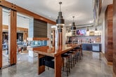 Located at 837 NW Donovan Rd in Lee's Summit, Missouri, this single-floor community lobby space blends industrial and modern design elements into a cohesive, welcoming environment. Polished concrete floors extend throughout, reflecting light and lending an open, contemporary feel to the entire area.

A centerpiece long bar-height communal table with a rich wood-toned surface is surrounded by metal and wood bar stools, creating a practical gathering and workspace. Overhead, a series of bold, tiered cylindrical pendant lights add dramatic visual interest while providing functional illumination. Exposed silver ductwork traces the ceiling, reinforcing the space's industrial aesthetic.

The service station along the back wall features dark cabinetry, a textured tile backsplash, a mounted flat-screen display, and a coffee and refreshment bar stocked for resident convenience. Gooseneck wall sconces accent this area with a nod to vintage industrial style.

Wood-clad structural columns with warm, natural grain detailing define zones throughout the space and anchor banks of black resident mailboxes set against walls featuring large-scale botanical murals. Barn-style sliding doors with heavy timber hardware separate the lobby from an adjacent lounge area, which is visible through the opening and offers comfortable seating and natural light from exterior windows. Together, these elements create a functional, stylish, and inviting community hub.