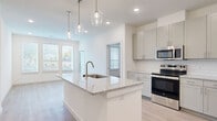 This thoughtfully designed 2-bedroom, 2-bathroom residence offers a bright and contemporary living experience across a single floor. The open-concept layout seamlessly connects the kitchen and living area, creating an inviting and functional space filled with natural light from multiple windows.

The kitchen serves as the heart of the home, anchored by a central island with a granite countertop and an undermount sink beneath elegant glass pendant lights. Sage-toned shaker cabinetry, a classic subway tile backsplash, and a full suite of stainless steel appliances — including a refrigerator, dishwasher, range, and microwave — complete this well-appointed space. A built-in shelving nook near the entry adds a practical touch.

The living area is open and airy, with large windows that frame outdoor views and allow abundant natural light to fill the room. Light wood-tone flooring flows consistently throughout the entire residence, lending warmth and cohesion to every space.

Both bedrooms are comfortably scaled and feature natural light, ceiling fans, and dedicated closets. The primary bedroom connects to a private en-suite bathroom with a granite-topped vanity, brushed nickel fixtures, and a marble-surround walk-in shower. The secondary bathroom mirrors this refined aesthetic, offering a granite vanity and a marble-surround tub-shower combination. A hallway and two closets round out the practical layout of this clean, modern residence.