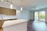 Located at 7595 W Atlantic Ave in Delray Beach, Florida, this single-story, 2-bedroom, 1-bathroom residence offers a well-designed open-concept layout with modern finishes throughout. Rich hardwood-style flooring flows consistently across the living areas and bedrooms, creating a cohesive and polished aesthetic.

The combined kitchen and living area serves as the heart of the home. The kitchen is outfitted with wood-toned cabinetry extending to the ceiling, stainless steel appliances including a refrigerator, range, microwave, and dishwasher, white quartz countertops, a tile backsplash, and a central island with pendant lighting overhead. Track lighting and additional pendant fixtures illuminate the space effectively. The living area features a ceiling fan and floor-to-ceiling sliding glass doors opening to a private balcony with tropical outdoor views.

The spacious primary bedroom includes multiple windows providing ample natural light and a ceiling fan. A generously sized walk-in closet with multi-tiered wire shelving provides extensive storage. The second bedroom is clean and bright with hardwood-style flooring. The full bathroom features dual undermount sinks, a wide white quartz vanity, ample cabinetry, a large mirror, and a shower/tub combination with a window.