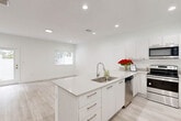 Located at 2741 NW 13th St in Pompano Beach, Florida, this two-story residence offers a clean, contemporary aesthetic defined by an all-white interior palette, light wood-look flooring, and recessed lighting throughout. The expansive main floor hosts the primary living areas, including an open-concept kitchen and living room designed for functionality and flow. The kitchen features a large center island with an undermount sink, white shaker-style cabinetry, quartz countertops, and a full suite of stainless steel appliances, including a refrigerator, range, microwave, and dishwasher. The adjoining living area provides generous open space bathed in natural light.

The hallway connects the main living spaces to the staircase, which leads to a more intimate upper level. The home includes four bedrooms, the primary of which is notably expansive, complemented by a walk-in closet with wire shelving systems. The three bathrooms maintain the home's modern style, featuring undermount sinks, quartz vanity surfaces, and large mirrors. A private balcony on the upper level overlooks the surrounding neighborhood and lush tropical greenery, adding an outdoor dimension to the living experience.