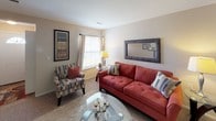 This single-floor residence offers a well-organized layout that efficiently connects its main living spaces. The living room serves as a comfortable central gathering area, featuring neutral carpet flooring, a window with blinds and curtains that allow natural light, and enough space to accommodate a sofa, accent chair, and glass coffee table. A large framed mirror on the wall adds depth to the room.

The dedicated dining area is positioned adjacent to the living space and features a round glass-topped table with seating for multiple guests, complemented by woven placemats and a decorative wall painting. Built-in storage with sliding doors is integrated nearby.

The galley-style kitchen includes white cabinetry, a gas range, refrigerator, double sink with countertop workspace, and stone-tile flooring. A doorway at the end leads to an in-unit laundry area.

The primary bedroom features carpet flooring, a window with sheer curtains, and direct access to a private bathroom equipped with a white vanity, mirror, and tub-shower combination. A second bedroom, similarly carpeted with natural light from a window, is served by a second full bathroom featuring a vanity with under-cabinet storage and a tub-shower combination with stone-tile flooring.