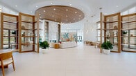 Located at 4331 34th St S in Saint Petersburg, Florida, this expansive single-floor amenity space showcases an exceptional coastal-modern design across a generously proportioned floor plan. The centerpiece of the space is a grand lobby featuring a striking circular wood-paneled ceiling, a dramatic marble fireplace surround flanked by built-in shelving, and a vibrant tropical mural that anchors an inviting lounge seating area. Large-format white porcelain tile flooring flows seamlessly throughout, reinforcing the bright, airy aesthetic.

Soaring ceilings and floor-to-ceiling windows dressed in sheer roller shades flood the interior with natural light while offering views of the surrounding outdoor areas. Slatted wood partitions and open shelving units elegantly define zones without sacrificing openness. A café-style bar area features a colorful geometric tile backsplash, counter seating with gold-accented stools, and stainless steel appliances.

A corridor lined with warm wood slat ceiling details leads to additional gathering areas, including intimate built-in seating nooks with slatted wood backdrops and pendant lighting, open co-working tables, and a glass-walled conference room. The overall ambiance is refined yet welcoming, blending coastal warmth with contemporary sophistication throughout every area of the space.