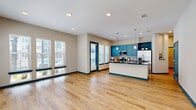 This thoughtfully designed 2-bedroom, 3-bathroom residence offers a comfortable and modern living experience across a single floor. The open-concept living room is a standout feature, showcasing warm light wood-style flooring, teal accent baseboards, and an abundance of natural light streaming through multiple large windows fitted with sleek white blinds. A door opens directly to views of the resort-style community pool area, seamlessly connecting indoor and outdoor living.

The kitchen is a visual centerpiece, featuring bold teal cabinetry, a striking dark granite island with pendant lighting, a patterned tile backsplash, and stainless steel appliances. Both bedrooms offer natural light via double windows, continuing the wood-style flooring and teal accent trim throughout. The primary bedroom includes a well-organized walk-in closet with wire shelving systems for ample storage.

The bathrooms are elegantly finished, with one featuring a soaking tub framed by full-height gray tile surround and brushed nickel fixtures. Another bathroom presents wood-look flooring, marble-style countertops, and built-in open shelving for practical storage. The residence also includes two closets and is part of a modern multi-story community with an expansive resort-style pool and lounge area.