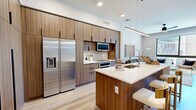 Located at 7450 N Uptown Dr in Tucson, AZ, this thoughtfully designed one-bedroom, one-bathroom residence offers a well-appointed single-floor layout that maximizes every square foot. The open-concept living and kitchen area serves as the heart of the home, where light wood-tone flooring flows seamlessly throughout. The kitchen is a standout feature, boasting warm walnut-finish cabinetry extending to the ceiling, stainless steel appliances including a French door refrigerator and built-in oven, a sleek white quartz waterfall island with bar seating, and a modern pendant light fixture overhead. The living room enjoys an abundance of natural light through oversized floor-to-ceiling windows that frame outdoor views, creating a bright and airy atmosphere ideal for relaxing or entertaining. The bedroom is a serene retreat, featuring large windows that invite natural light and offer exterior views, with light-toned walls and warm wood flooring contributing to a calm, neutral palette. The bathroom is finished to a high standard, with large-format gray tile in the glass-enclosed walk-in shower, a floating vanity with white quartz countertop, an illuminated mirror, and wood-look tile flooring. A dedicated closet and hallway complete this efficiently designed, contemporary residence.