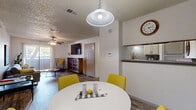This thoughtfully arranged 1-bedroom, 2-bathroom residence offers a practical and stylish single-floor layout. The living room features wood-look flooring, a textured ceiling, and a ceiling fan with lighting. A large sliding glass door dressed with vertical blinds floods the space with natural light and provides outdoor views. Adjacent to the living area, the dining room is defined by a teal accent wall, a pendant light fixture, and wood-look flooring that continues throughout. A pass-through connects the dining area to the kitchen, which features granite-style countertops and light cabinetry. The bedroom is carpeted for comfort, includes a ceiling fan, a natural-light window with blinds, and a soft blue accent wall. A dedicated closet provides additional storage. The primary bathroom is well-appointed with a wide vanity, gray cabinetry, granite-style countertops, a large framed mirror, and wood-look tile flooring. A second bathroom features a full tub-and-shower combination with clean white tile surround. Throughout the unit, textured ceilings, neutral walls, and consistent flooring choices create a cohesive and functional living environment.