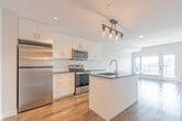 Located at 98 Farley Dr in Guelph, Ontario, this thoughtfully designed one-bedroom, one-bathroom unit offers a efficient and modern living experience across a single floor. The open-concept layout is anchored by a contemporary kitchen featuring crisp white cabinetry, dark granite-style countertops, a central island with an undermount sink and gooseneck faucet, and a full suite of stainless steel appliances including a refrigerator, electric range, and over-the-range microwave. An industrial-style pendant light fixture adds a stylish focal point above the island. Wood-look vinyl plank flooring runs throughout the unit, providing warmth and visual continuity. The bedroom is a comfortable, well-proportioned space bathed in natural light from a large window overlooking a treed outdoor setting with views of the surrounding Guelph skyline. Clean white walls and neutral tones create a calm, airy atmosphere. Two interior doors in the bedroom provide access to closet and hallway spaces. The bathroom is finished with white tile, a soaker tub with shower, a white vanity with dark countertop, and a large mirror with overhead lighting, maintaining the unit's cohesive modern aesthetic throughout.