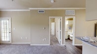 This efficiently designed one-bedroom, one-bathroom unit offers a thoughtfully organized layout across a single floor. The living room serves as the heart of the space, featuring plush carpeting, crown molding, and a large window alongside a glass-paneled door that fills the room with natural light. An open pass-through connects the living area to the kitchen, which is outfitted with white cabinetry, laminate countertops, a stainless steel refrigerator, and a black electric range beneath a ventilation hood — all set on durable wood-style flooring.

The bedroom is a comfortable retreat, carpeted and finished with crown molding, and includes access to a generously sized walk-in closet equipped with wire shelving systems on multiple walls. A notable built-in desk nook with overhead shelving adds functional workspace. The full bathroom features a soaking tub with a tiled surround accented by decorative tiles, complemented by overhead cabinetry for storage. A dedicated laundry area includes washer/dryer hookups and an overhead wire shelf, adding practicality to the overall layout. Warm neutral tones and consistent finishes throughout create a cohesive, understated ambiance.