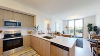 Located at 2512 NE 181st St in North Miami Beach, FL, this well-appointed 2-bedroom, 2-bathroom residence offers a thoughtfully designed single-floor layout with a clean, contemporary aesthetic. The open-concept kitchen and living area serves as the heart of the home, featuring light wood cabinetry, a marble-style tile backsplash, stainless steel appliances, and a sleek white quartz peninsula with bar seating — ideal for both cooking and entertaining. The living area flows seamlessly toward floor-to-ceiling sliding glass doors that open onto a private balcony, inviting abundant natural light and framing lush outdoor views. Light hardwood-style flooring and crisp white walls create a bright, airy ambiance throughout. The primary bedroom offers a comfortable retreat with large windows overlooking the greenery below, while the second bedroom mirrors the same bright, serene character. Both bathrooms are finished with modern wood-toned vanities and white quartz countertops; the primary bath features a standout glass-enclosed walk-in shower clad in full marble-style tile. Four closets and a dedicated utility room provide generous storage. This residence combines modern design with functional livability in a vibrant South Florida setting.