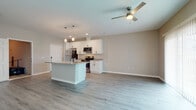 Located at 3301 Whitney Rd in Largo, FL, this two-story townhome offers a clean, contemporary design throughout. The open-concept main living area seamlessly connects the kitchen and living room, creating a bright and functional space filled with natural light from large sliding glass doors fitted with vertical blinds. Light-toned luxury vinyl plank flooring runs throughout, complementing the neutral wall palette of soft grays and warm beiges.

The kitchen is a standout feature, showcasing white shaker-style cabinetry with matte black hardware, granite countertops, a center island with a built-in sink and pendant lighting overhead, and a full suite of stainless steel appliances including a range, microwave, dishwasher, and refrigerator. A ceiling fan anchors the living area, which benefits from generous natural light.

A half bathroom on the main level features a granite-topped white vanity and a round mirror. An in-unit laundry closet houses a full-size washer and dryer. The attached garage offers private, convenient parking with an automatic door opener. Upper-level spaces continue the consistent modern finishes seen throughout the home. This well-appointed townhome combines practical amenities with stylish details in a move-in-ready package.
