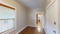 Located on NW Overton Street in Portland, Oregon, this efficient one-bedroom, one-bathroom unit offers a well-organized single-floor layout. The bedroom is the largest room in the unit, featuring rich hardwood floors, warm neutral-toned walls, crown molding, and white wood-trimmed windows fitted with blinds. Two windows allow natural light to fill the space while offering views of the surrounding neighborhood greenery. Crown molding runs throughout, adding a classic architectural touch that elevates the interior's character. The compact kitchen is thoughtfully designed with warm wood cabinetry, open shelving, a gas range, a full-size refrigerator, and a single-basin sink with a modern faucet. A window above the counter brings in additional natural light. The bathroom features a walk-in shower enclosed by a glass sliding door with chrome hardware, white surround panels, and a small transom window for ventilation and light. Light tile flooring and neutral walls give the bathroom a clean, functional feel. Throughout the unit, consistent use of hardwood and light-toned flooring, neutral wall colors, and white trim creates a cohesive and understated aesthetic well-suited to urban living in the heart of Portland's Northwest neighborhood.
