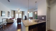 This single-floor residence is designed with an open-concept layout that seamlessly connects the kitchen and living areas, creating a cohesive and functional living space. The kitchen is well-appointed with dark espresso cabinetry, granite countertops, a mosaic tile backsplash, and stainless steel appliances including a refrigerator, range, and microwave. A kitchen island with a built-in sink and pendant lighting above serves as both a prep space and a visual divider between the kitchen and living area. Dark wood-style flooring runs throughout the main living spaces, adding warmth and continuity.

The living room benefits from natural light provided by French doors that open to a balcony, complemented by a ceiling fan and patterned drapes. The space is comfortably sized to accommodate a full seating arrangement.

The primary bedroom features plush carpeting, large windows that invite natural light, a ceiling fan, and ample space for a full furniture suite. A second bedroom similarly offers carpeted flooring and bright window coverage. The bathroom includes a granite-topped vanity with dark cabinetry, a combination tub and shower, wood-style flooring, and direct access to a walk-in closet.